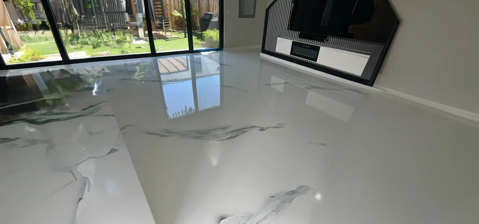 Mirror-finish metallic epoxy living-room floor in a Weston home, with white marbling and glass doors onto the garden