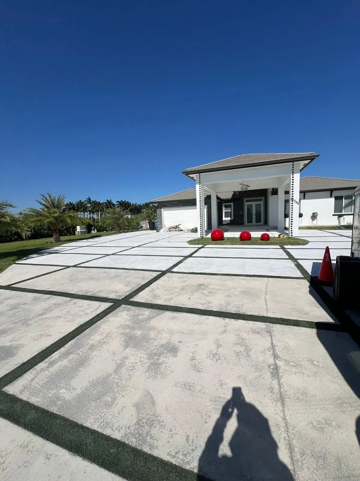 Before coating: bare grey concrete driveway pads with the artificial turf strips already in place, in front of the house and pergola