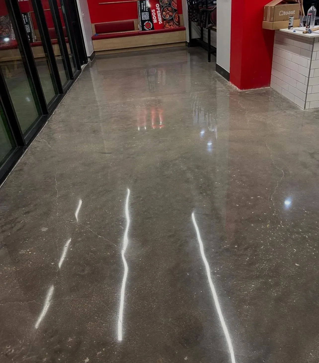 Freshly polished concrete floor in a pizza restaurant, high-gloss grey slab reflecting the ceiling lights, red walls and a white tile counter