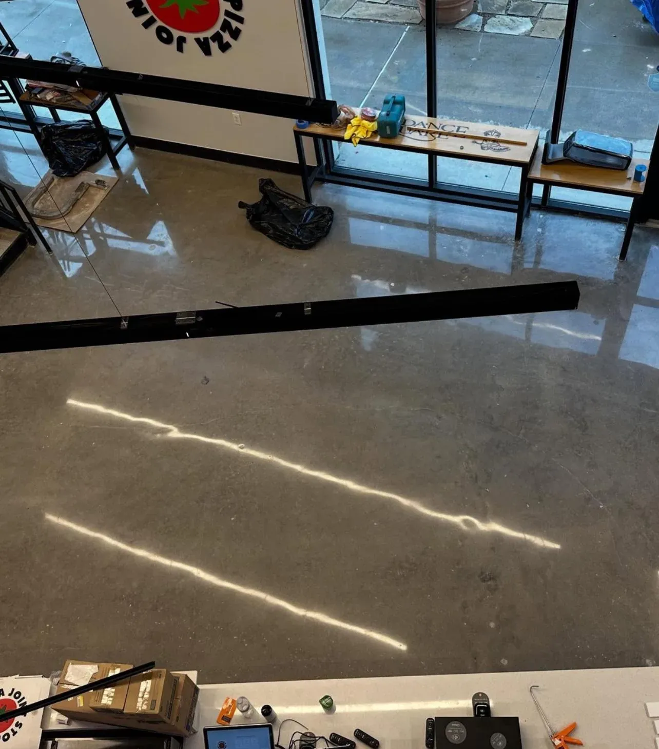 Polished concrete restaurant floor seen from above during fit-out, light reflections across the slab and the storefront windows behind