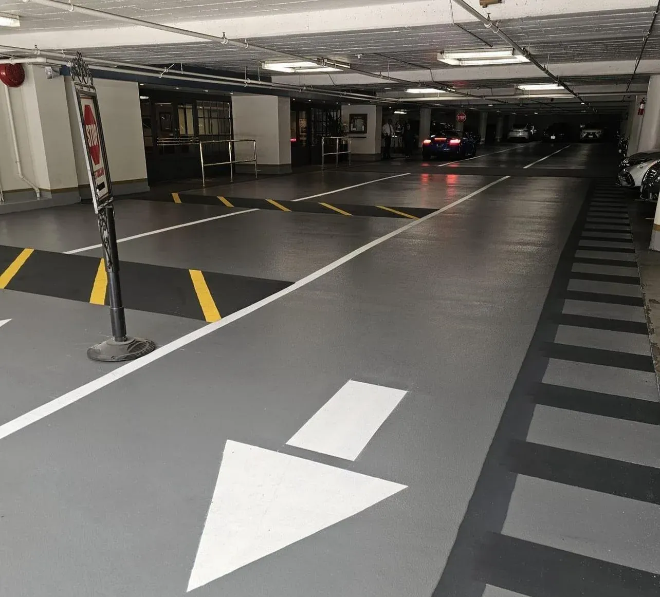 Indoor parking garage with a grey traffic coating, white lane arrows, yellow hatched no-parking zones and dark grey striping