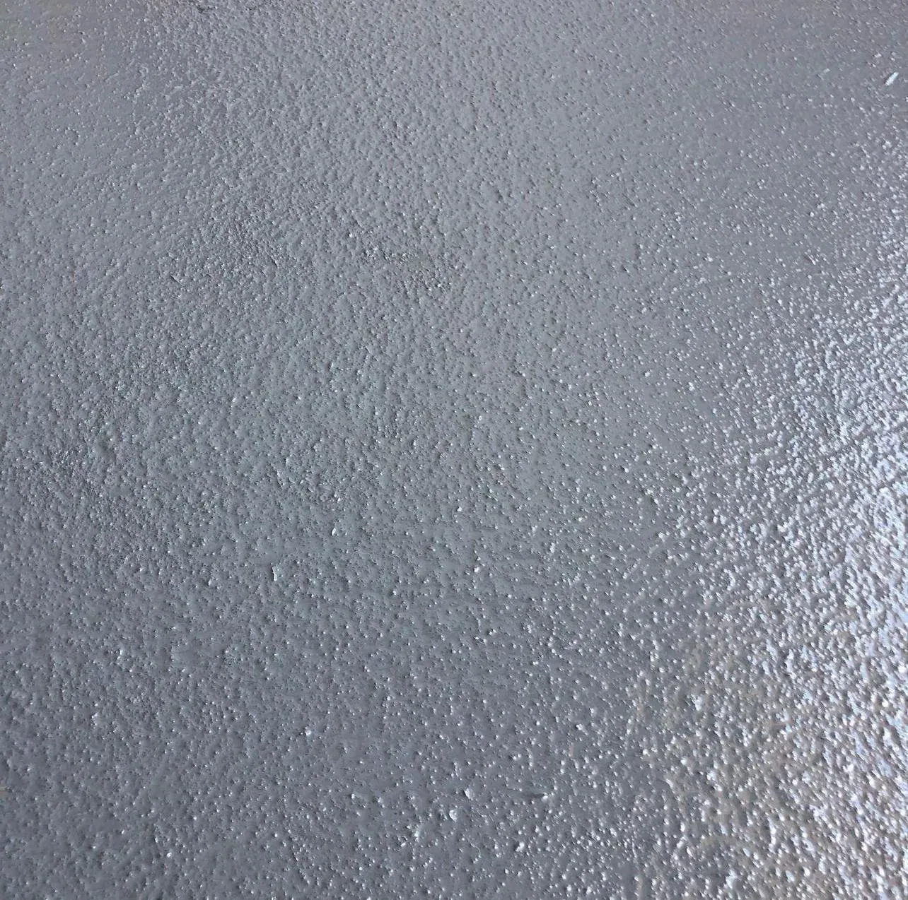 Close-up of a grey slip-resistant textured coating on a concrete deck, showing the aggregate grain that gives grip when wet